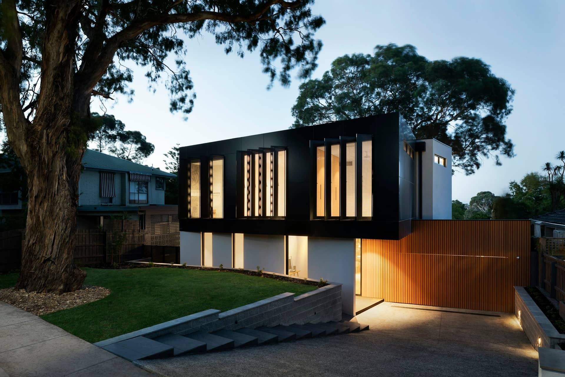 Modern black-and-timber home with glowing windows at dusk