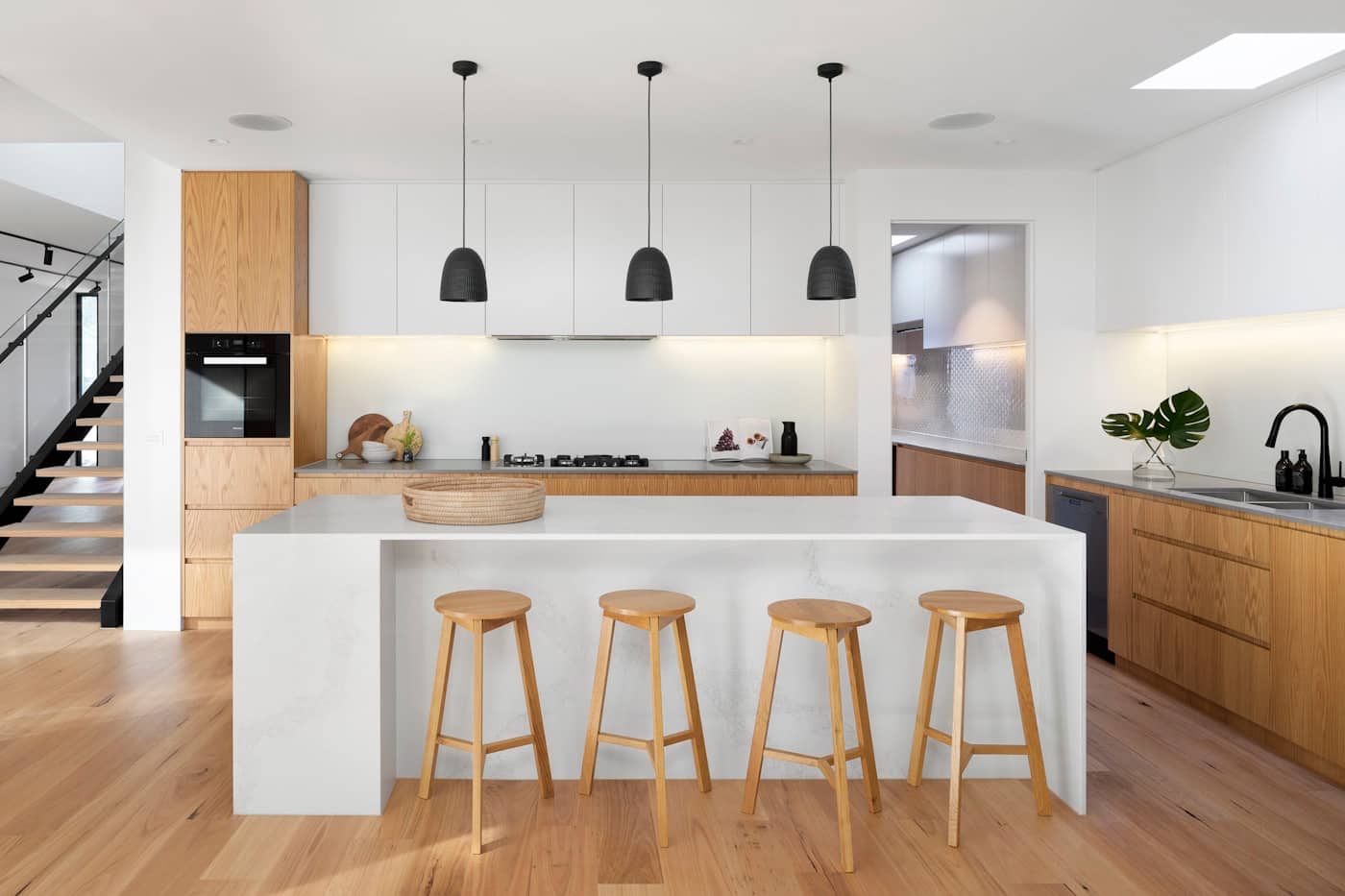 White-and-oak kitchen with island seating and black pendant lights